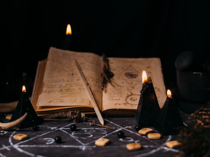 Open old book with magic spells, runes, black candles on witch table. Occult, esoteric, divination and wicca concept.